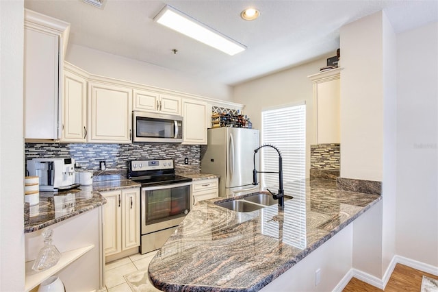 kitchen featuring kitchen peninsula, dark stone countertops, stainless steel appliances, and cream cabinets