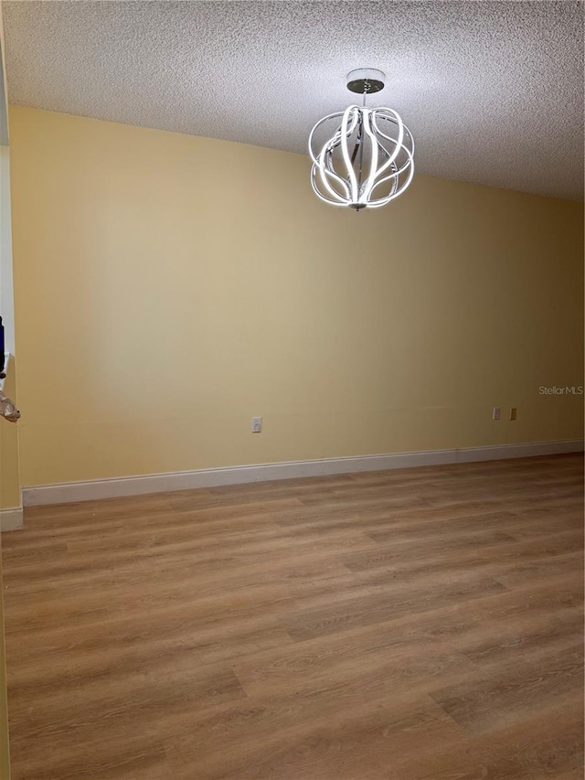 unfurnished room featuring wood-type flooring, a textured ceiling, and a notable chandelier