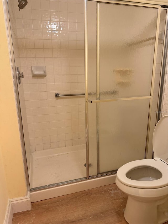 bathroom with toilet, a shower with door, and hardwood / wood-style flooring