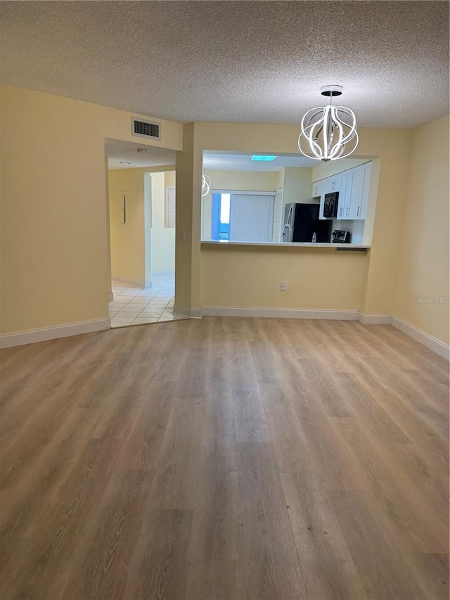 unfurnished living room with a textured ceiling, light hardwood / wood-style flooring, and a chandelier