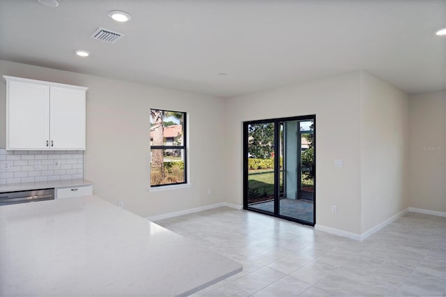 interior space featuring light tile patterned floors, backsplash, white cabinets, and dishwasher