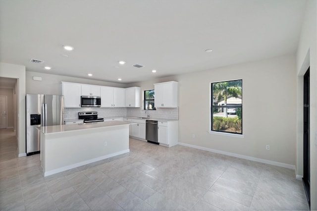 kitchen with stainless steel appliances, light tile patterned flooring, a kitchen island, white cabinets, and sink