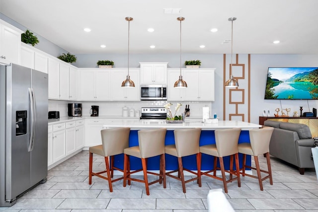 kitchen featuring stainless steel appliances, decorative light fixtures, a kitchen breakfast bar, and an island with sink