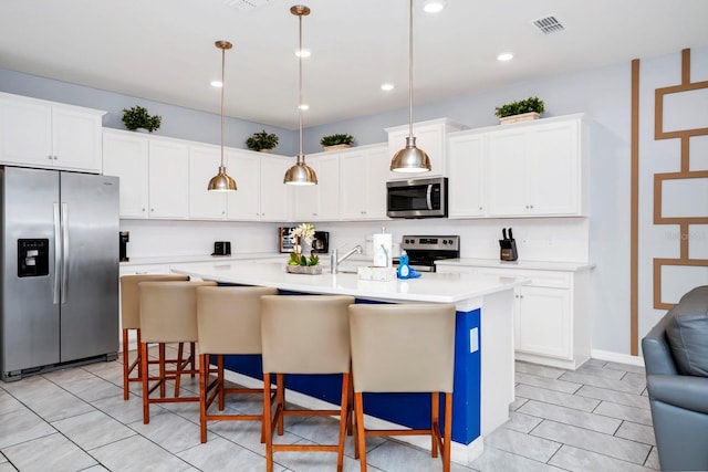 kitchen with pendant lighting, stainless steel appliances, white cabinets, and a center island with sink