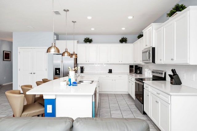 kitchen featuring decorative light fixtures, stainless steel appliances, an island with sink, and white cabinets