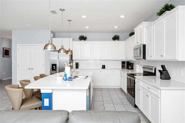 kitchen featuring appliances with stainless steel finishes, decorative light fixtures, a center island with sink, and white cabinets