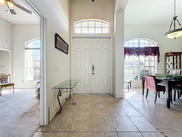 carpeted entryway featuring ceiling fan, a healthy amount of sunlight, and a towering ceiling