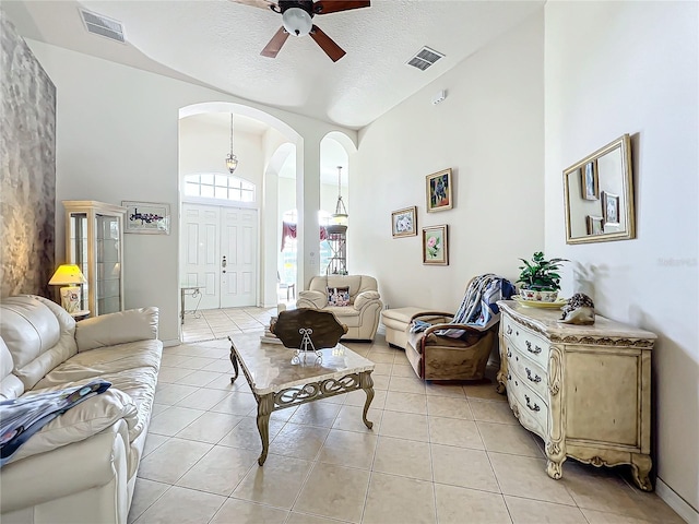 tiled living room featuring ceiling fan, a high ceiling, and a textured ceiling