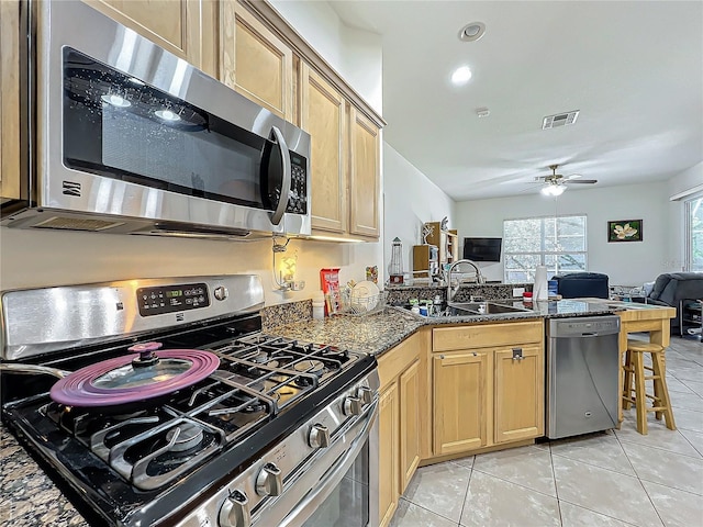 kitchen featuring appliances with stainless steel finishes, dark stone counters, sink, a kitchen breakfast bar, and light tile patterned floors