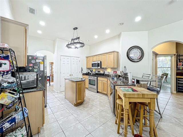 kitchen featuring a center island, hanging light fixtures, appliances with stainless steel finishes, light tile patterned floors, and dark stone counters