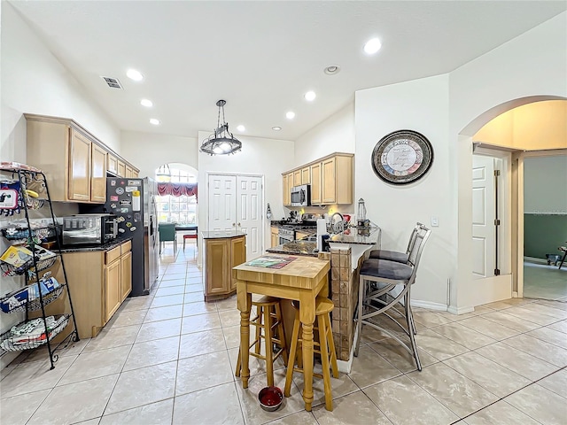 kitchen with light brown cabinetry, light tile patterned flooring, stainless steel appliances, and pendant lighting