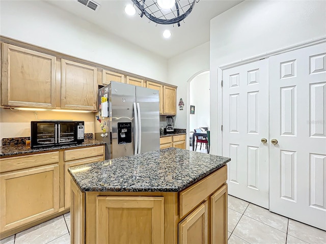 kitchen featuring light tile patterned flooring, dark stone countertops, stainless steel fridge with ice dispenser, and a kitchen island