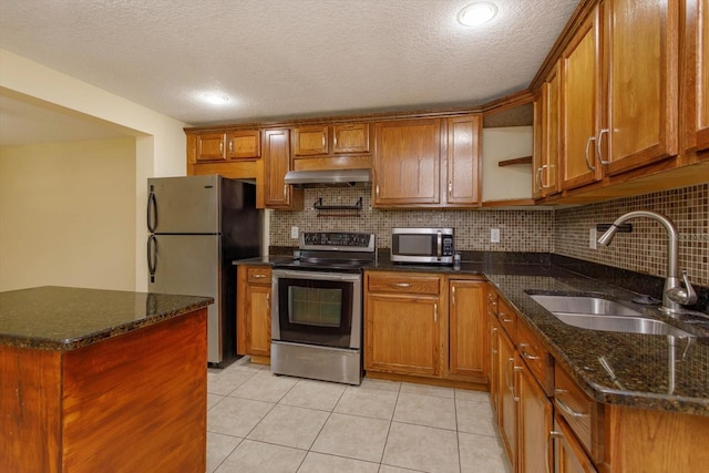 kitchen featuring light tile patterned floors, appliances with stainless steel finishes, dark stone counters, range hood, and sink