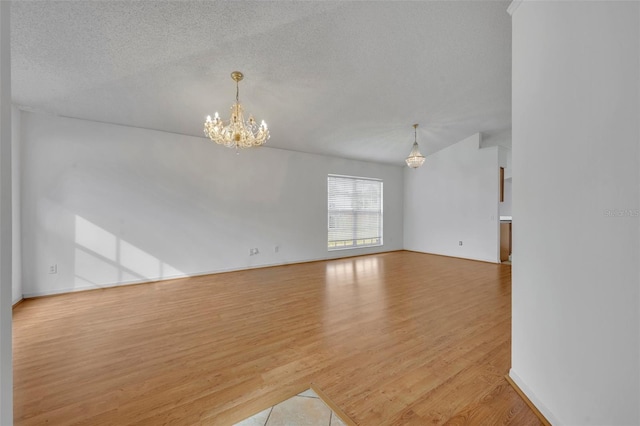 spare room featuring a notable chandelier, a textured ceiling, and light hardwood / wood-style flooring