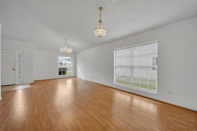 spare room featuring light wood-type flooring, a chandelier, and a textured ceiling