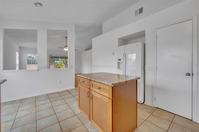 kitchen featuring ceiling fan, light tile patterned flooring, white fridge with ice dispenser, light stone countertops, and a center island