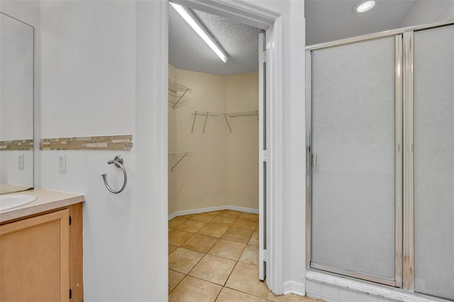 bathroom with a textured ceiling, tile patterned flooring, a shower with shower door, and vanity