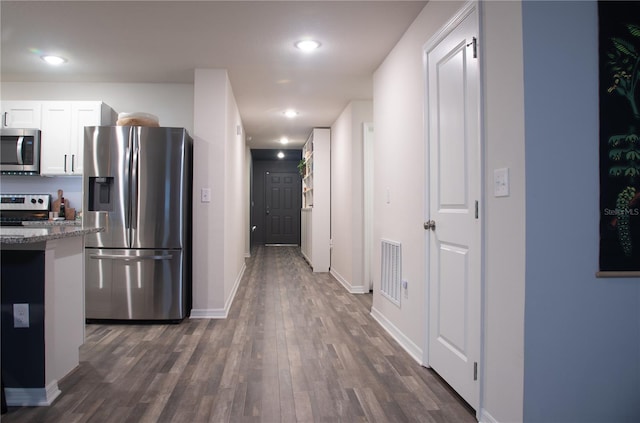 kitchen with dark wood-type flooring, white cabinets, appliances with stainless steel finishes, and stone countertops