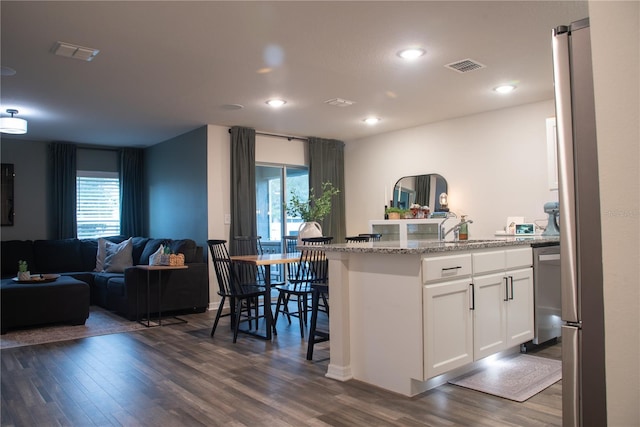 kitchen featuring white cabinets, a kitchen breakfast bar, dark hardwood / wood-style floors, light stone counters, and stainless steel dishwasher