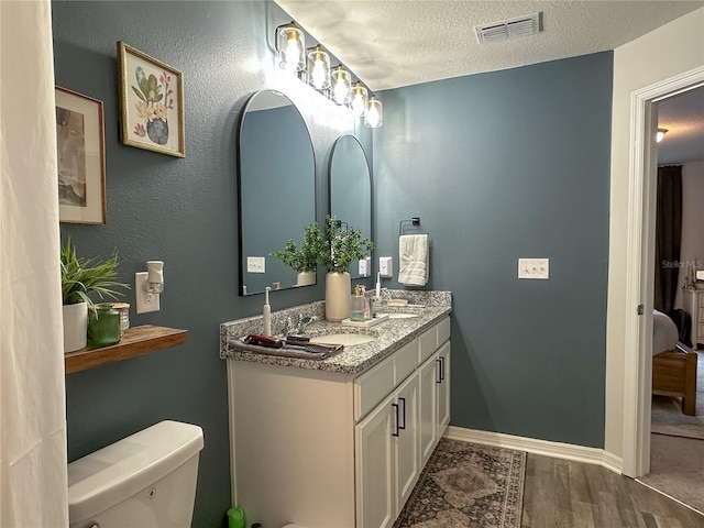 bathroom with wood-type flooring, a textured ceiling, toilet, and vanity