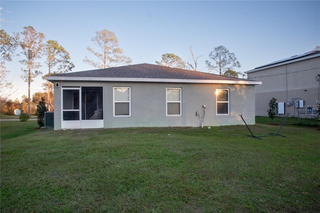 back house at dusk with a yard and central AC unit