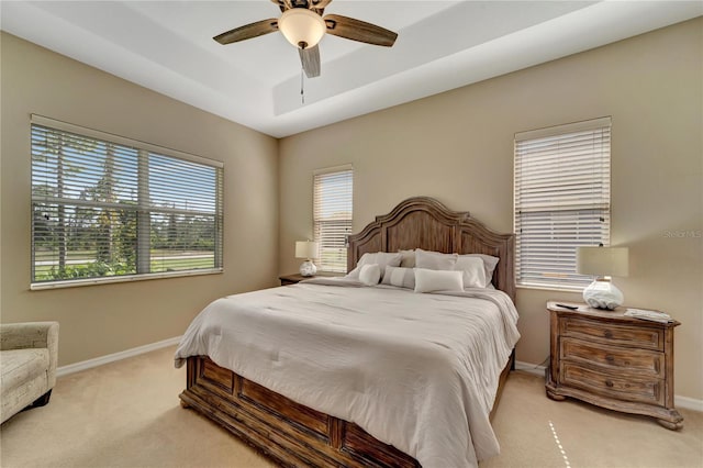 bedroom featuring ceiling fan, light carpet, and a tray ceiling