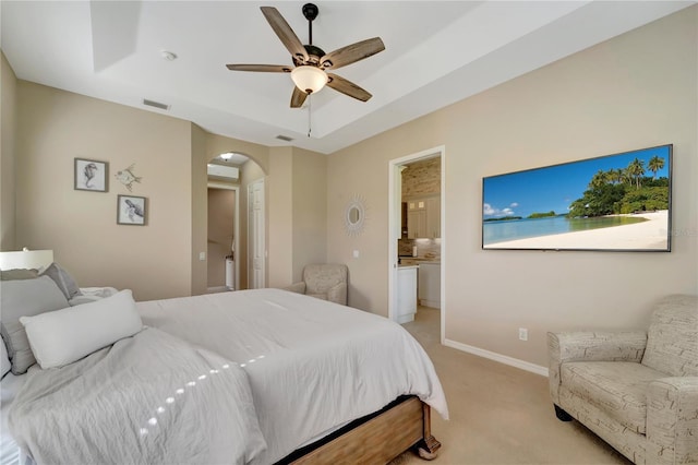 carpeted bedroom with ceiling fan, ensuite bathroom, and a raised ceiling