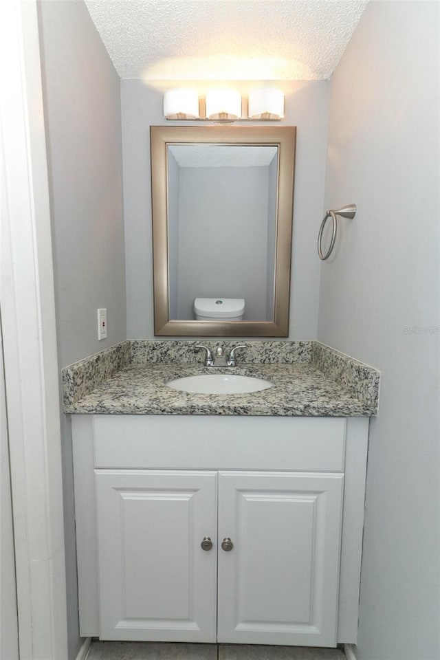 bathroom featuring a textured ceiling, toilet, and vanity