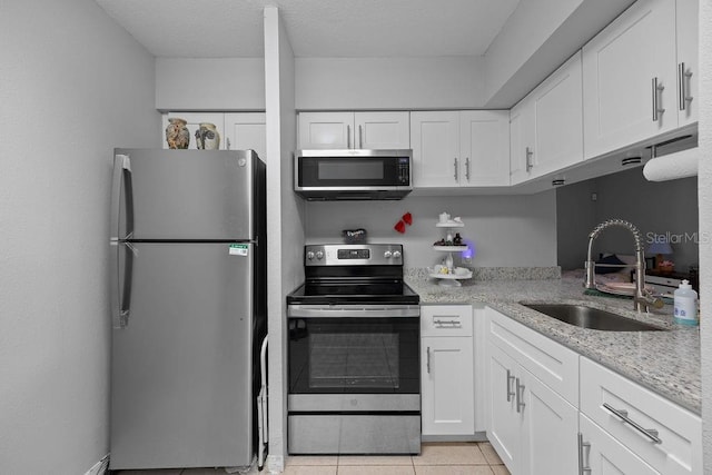 kitchen with light tile patterned floors, white cabinetry, stainless steel appliances, light stone countertops, and sink