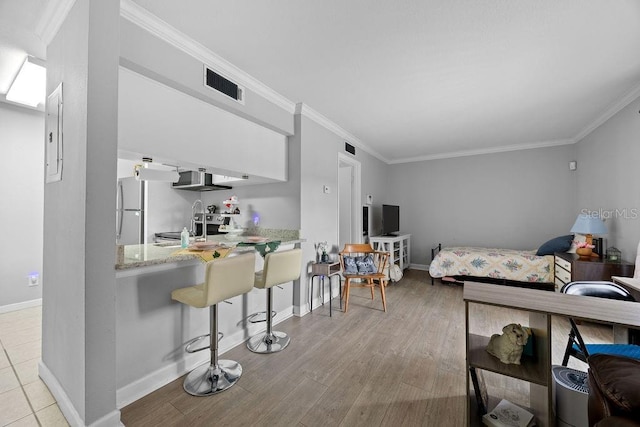 bedroom with crown molding, light hardwood / wood-style flooring, fridge, and sink