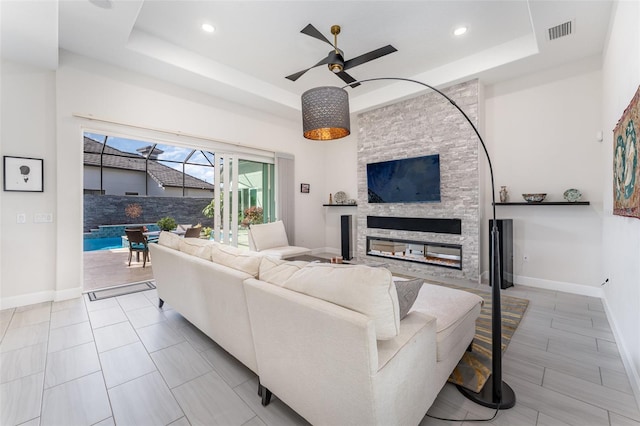 living room featuring ceiling fan, a raised ceiling, and a fireplace