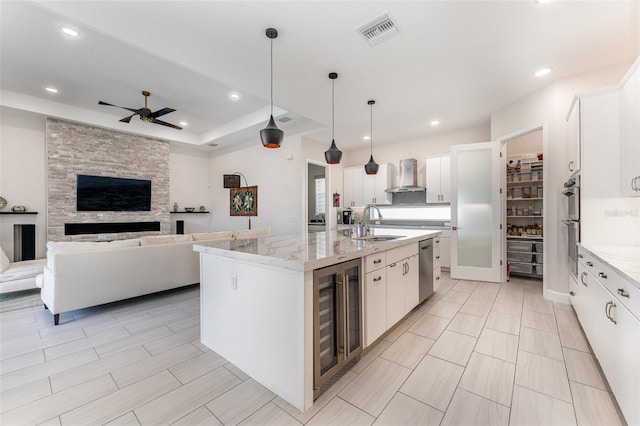 kitchen featuring white cabinets, an island with sink, wall chimney range hood, and beverage cooler