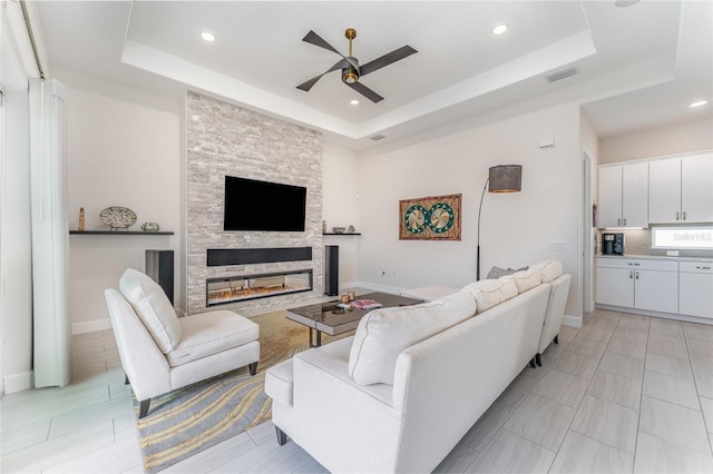 living room featuring ceiling fan, a fireplace, and a tray ceiling