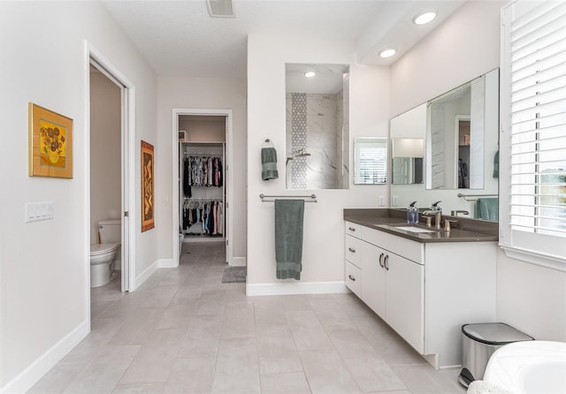 bathroom with toilet, vanity, a tile shower, and tile patterned flooring