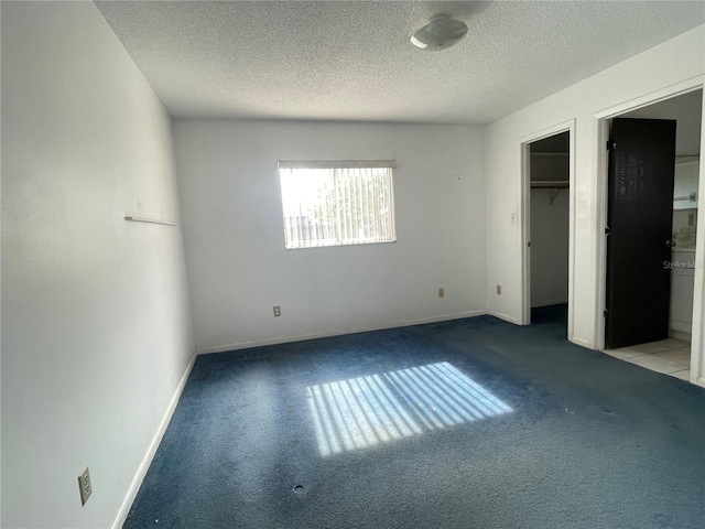 unfurnished bedroom featuring ensuite bathroom, light colored carpet, a spacious closet, and a textured ceiling