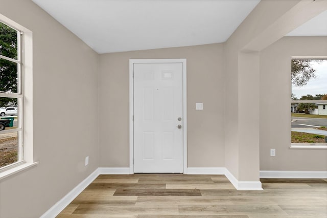 foyer entrance featuring plenty of natural light, vaulted ceiling, and light wood-type flooring