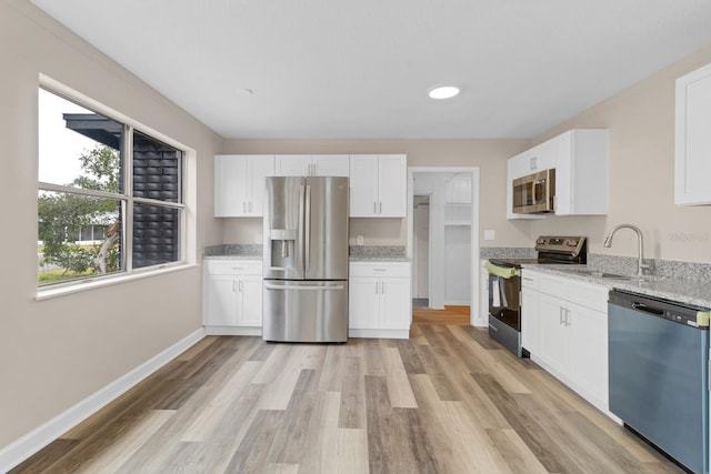 kitchen with sink, light stone counters, stainless steel appliances, and white cabinetry