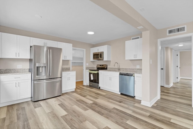 kitchen featuring light wood-type flooring, appliances with stainless steel finishes, white cabinetry, and light stone countertops