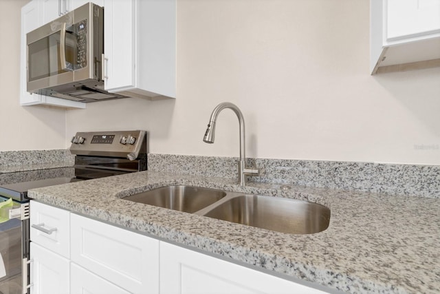 kitchen with light stone counters, sink, white cabinets, and appliances with stainless steel finishes