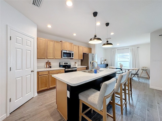 kitchen with pendant lighting, stainless steel appliances, an island with sink, sink, and a kitchen breakfast bar