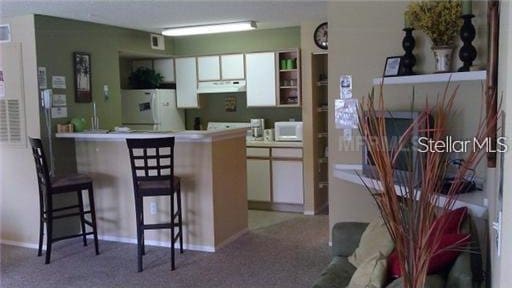 kitchen with a breakfast bar, white cabinetry, kitchen peninsula, and fridge