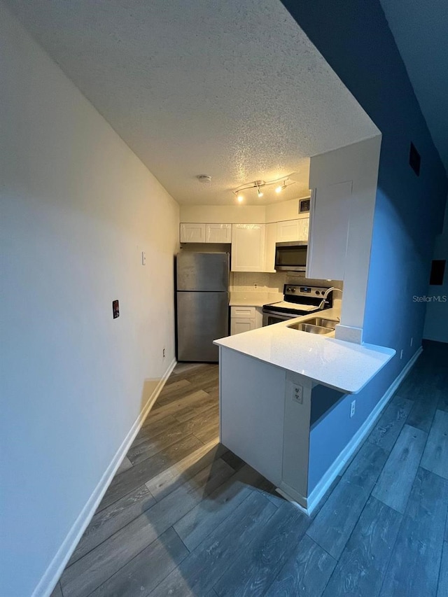 kitchen with white cabinetry, hardwood / wood-style flooring, kitchen peninsula, appliances with stainless steel finishes, and a textured ceiling