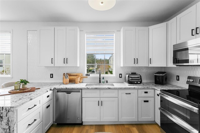 kitchen with appliances with stainless steel finishes, white cabinets, light wood-type flooring, sink, and light stone counters