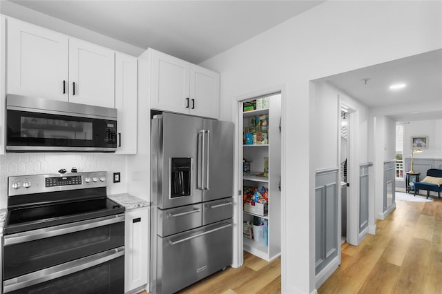 kitchen with light hardwood / wood-style floors, light stone counters, white cabinets, and stainless steel appliances