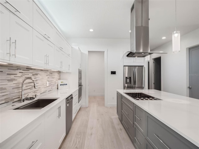 kitchen with pendant lighting, appliances with stainless steel finishes, white cabinetry, island exhaust hood, and sink