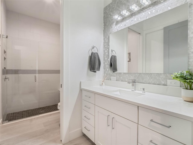 bathroom with wood-type flooring, vanity, backsplash, toilet, and a shower with shower door