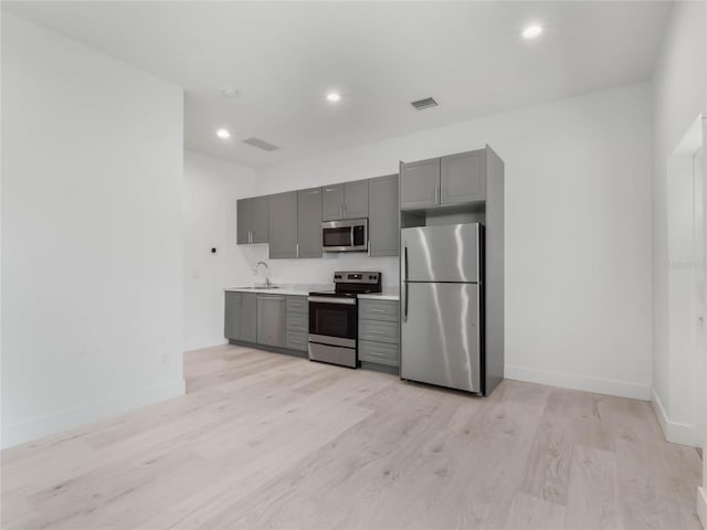 kitchen with light wood-type flooring, sink, gray cabinetry, and stainless steel appliances