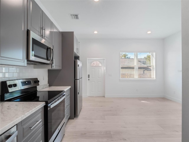 kitchen featuring light hardwood / wood-style flooring, stainless steel appliances, backsplash, light stone counters, and gray cabinetry