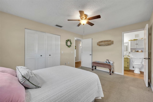 bedroom featuring ceiling fan, ensuite bathroom, a textured ceiling, light colored carpet, and a closet