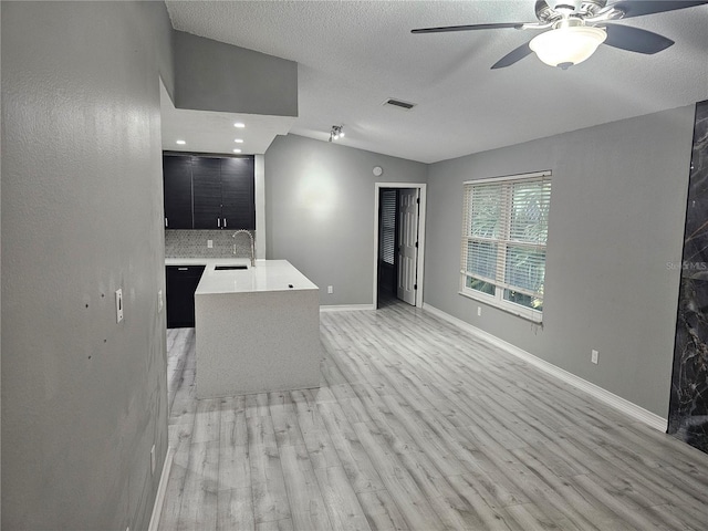 unfurnished living room with ceiling fan, vaulted ceiling, sink, and light hardwood / wood-style floors